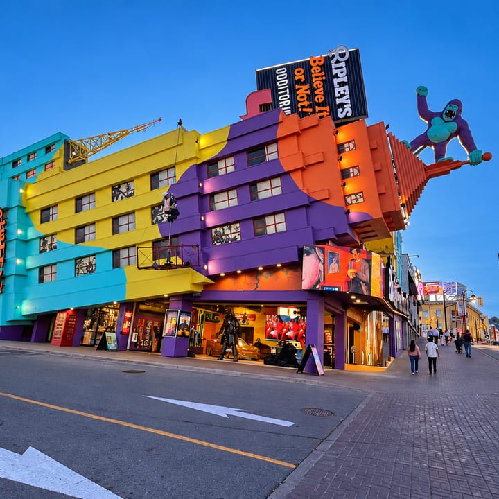 A brightly painted building in yellow, teal, purple and orange panels, topped with a giant gorilla figure and a Ripley's Believe It or Not! sign, stands on a street at blue hour.