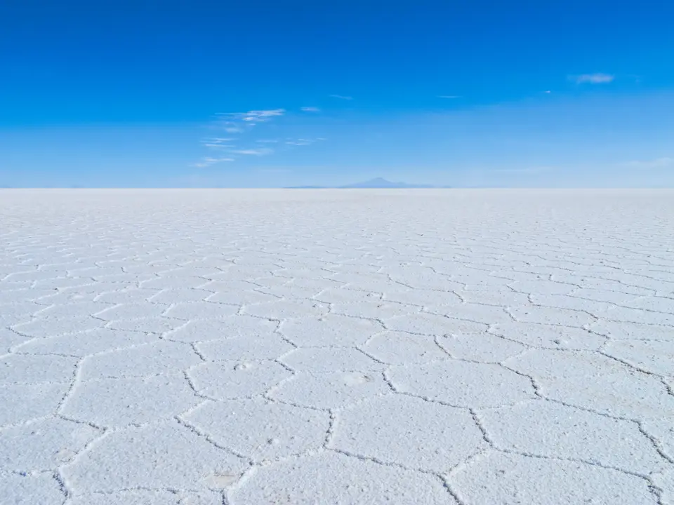 The dry Salar de Uyuni: a white plain of hexagonal salt ridges under a blue sky.