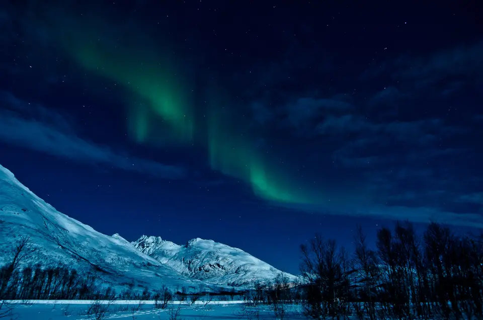Green northern lights above a snowy mountain ridge and fjord in northern Norway.