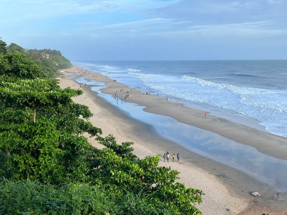 A long beach with waves and a green headland at Papanasam beach, Varkala.