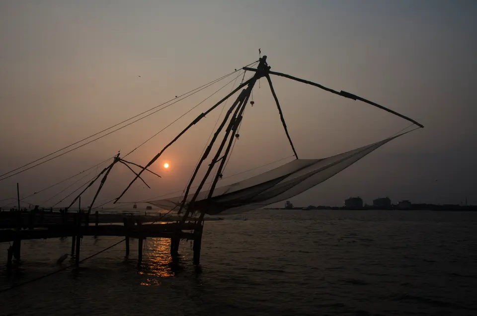 A Chinese fishing net silhouetted against the setting sun over the water at Fort Kochi.