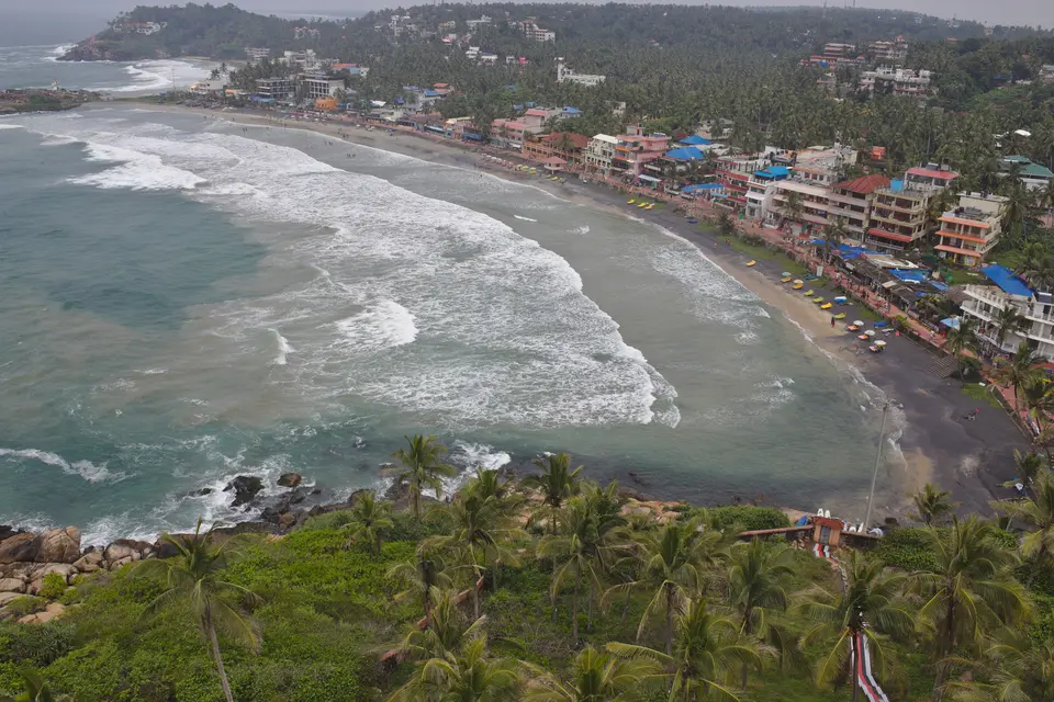 A curved beach with surf and a town beside it seen from a green headland at Kovalam.