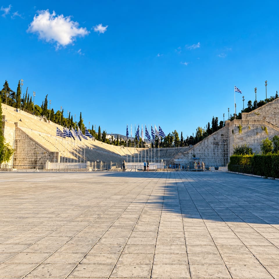 The Panathenaic Stadium seen from the paved square in front of it: tiers of marble seating, a row of Greek flags and cypress trees on the hillside.