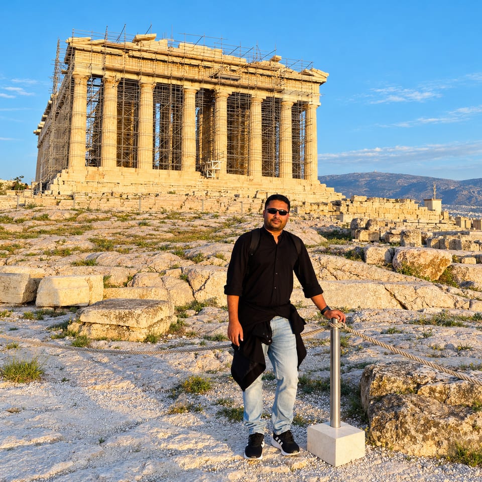 The traveller stands on the rocky top of the Acropolis in evening light, in front of the Parthenon, which is partly covered in scaffolding.